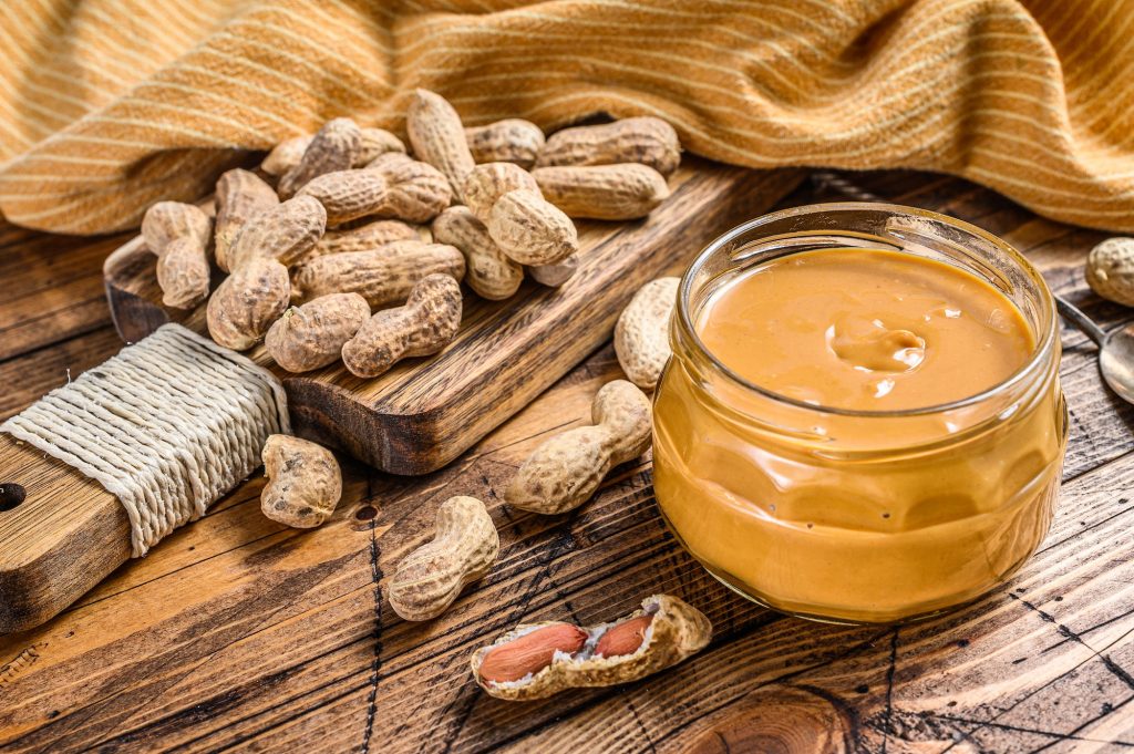 Fresh made creamy Peanut Butter in a glass jar. Wooden background. Top view